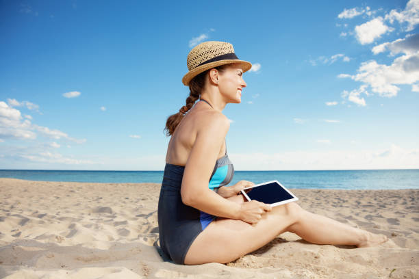 istock smiling young woman in swimsuit with tablet PC on beach 1027673654