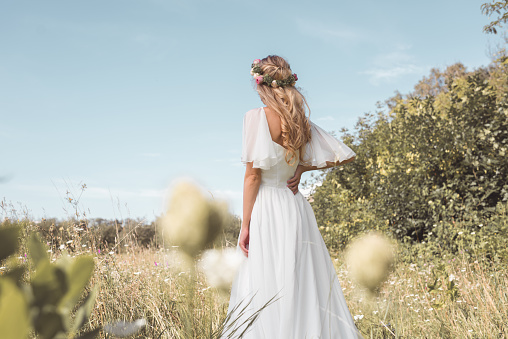 back view of tender young blonde bride walking on beautiful field