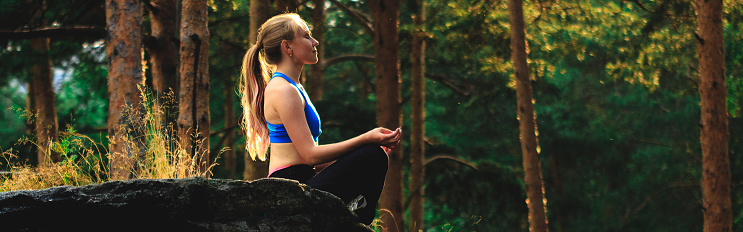 Blonde woman doing exercises outdoors on a rock in the forest. Yoga nature concept