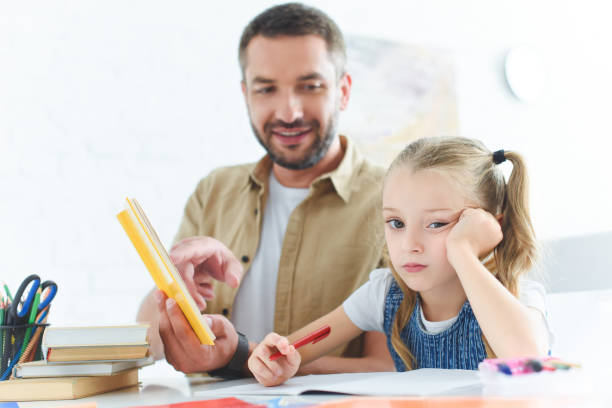 istock father and bored daughter doing homework together at home 1027680498