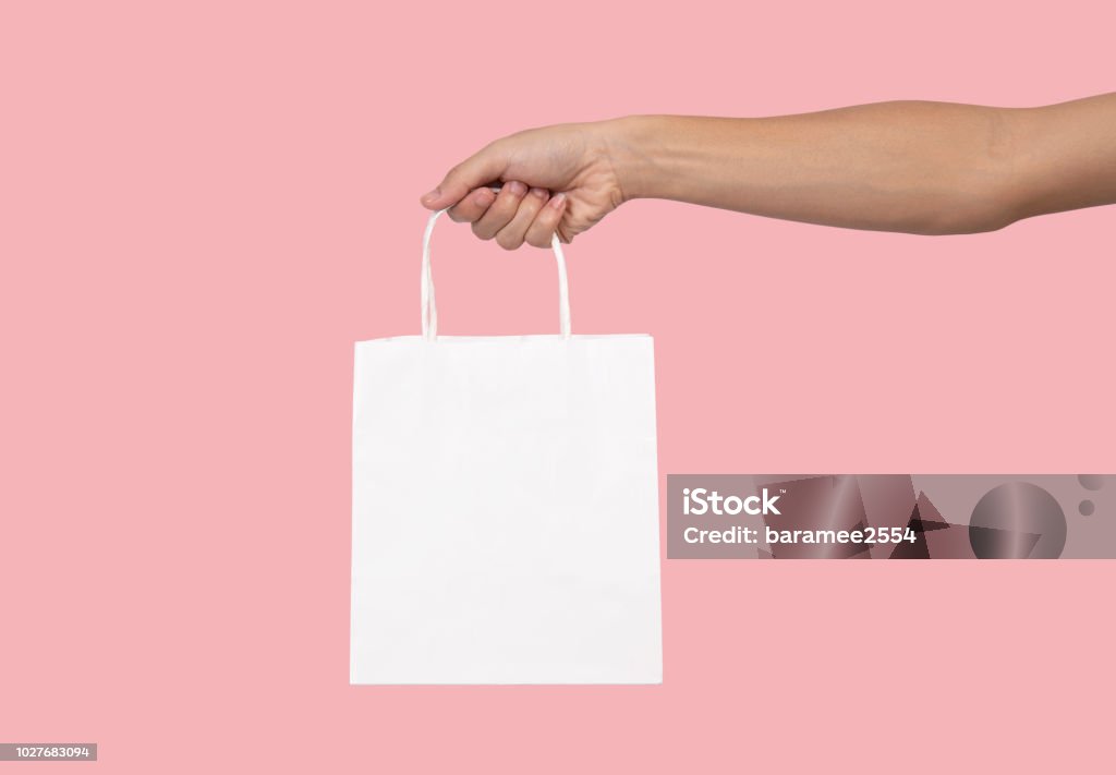 Hand holding blank white paper bag for mockup template advertising and branding isolated on pink background. Hand Stock Photo