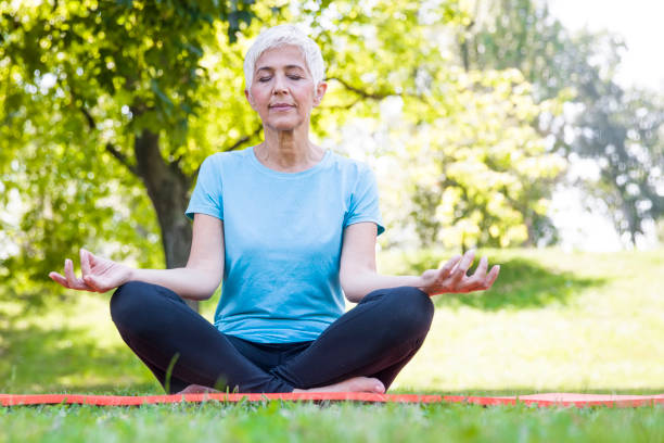 istock Senior woman in lotus pose sitting on green grass 1027690480