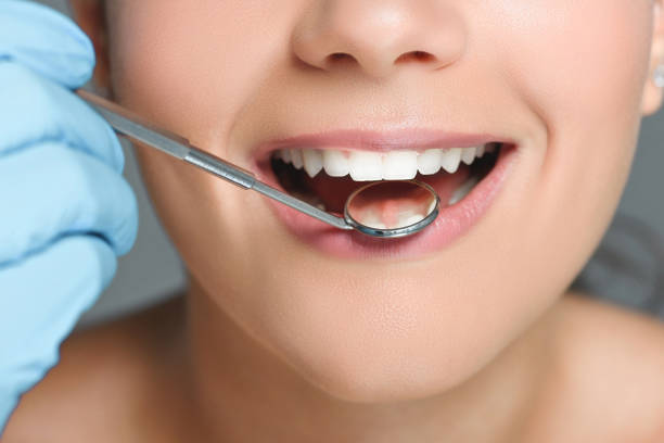 istock partial view of dentist with dental mirror checking womans teeth 1027691018