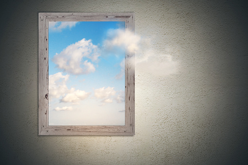 think outside the box concept with picture frame with bright sky with clouds inside at concrete wall background