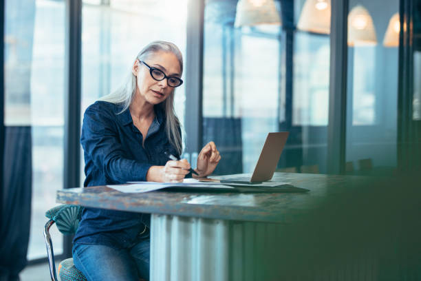 Senior businesswoman working at office Portrait of senior woman sitting at table in office and reading few paper work. Business manager working on some documents at office. business lifestyle stock pictures, royalty-free photos & images