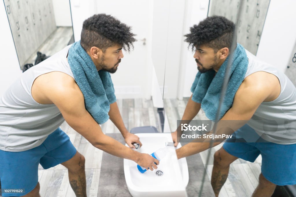 I'm Gonna Reach My Goal Today! Young man pouring water into the bottle and looking at the mirror, preparing for a training session at the gym locker room. Mirror - Object Stock Photo
