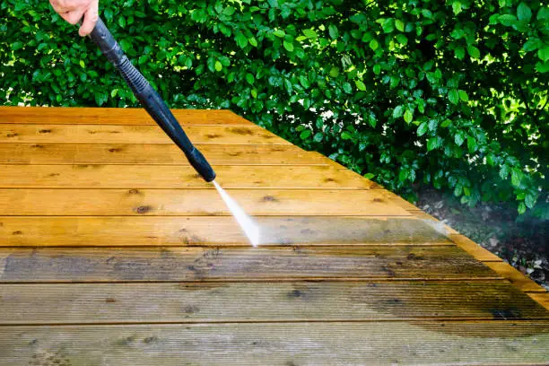Photo of cleaning terrace with a power washer - high water pressure cleaner on wooden terrace surface