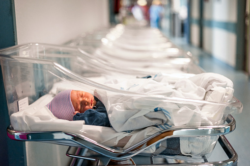 Newborn baby boy in his small transparent portable hospital bed
