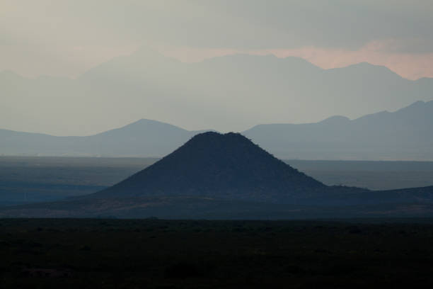 One lone, perfectly formed hill, amount tall mountains, at sunset.