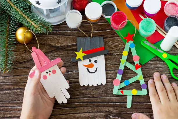 A child is holding Christmas decoration or Christmas gift wooden sticks. Handmade. Project of children's creativity, handicrafts, crafts for kids.