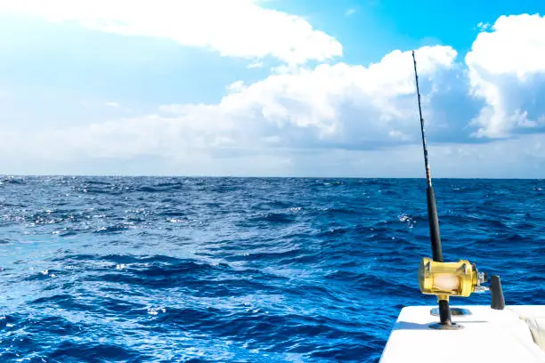 Photo of Fishing rod in a saltwater private motor boat during fishery day in blue ocean. Successful fishing concept