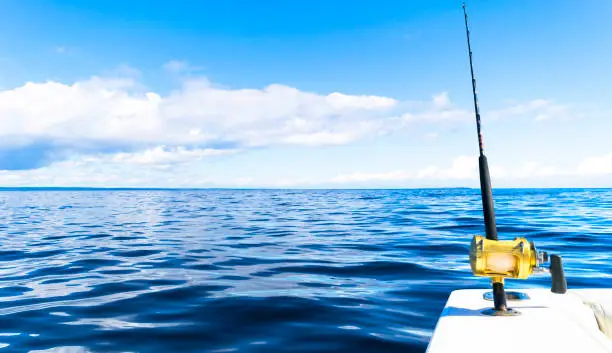 Photo of Fishing rod in a saltwater private motor boat during fishery day in blue ocean. Successful fishing concept