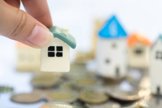 istock Woman's hand putting house model on coins stack. Concept for property ladder, mortgage and real estate investment . 1027747044