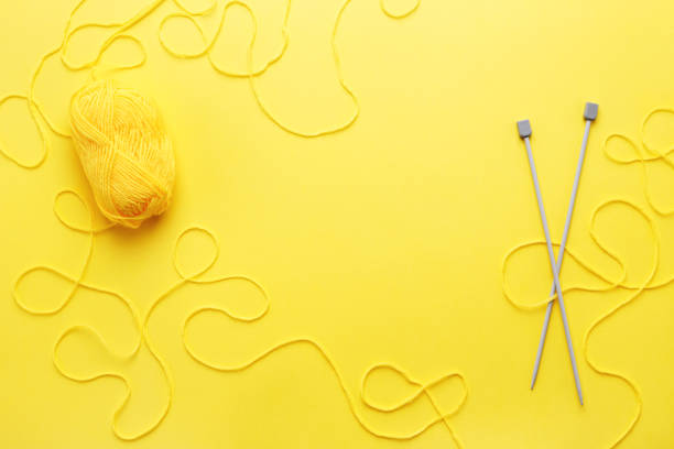 Yellow yarn skein, knitting needles and frame of tangled woolen thread on yellow table. Flat lay, hobby or needlework concept.