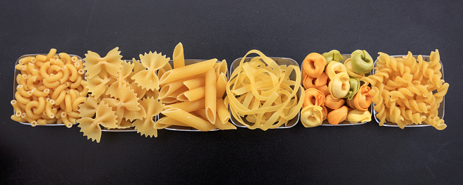 Row of various shapes of pasta on a black background
