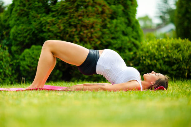 donna incinta che pratica la posa del ponte sull'erba - human pregnancy exercising relaxation exercise sport foto e immagini stock