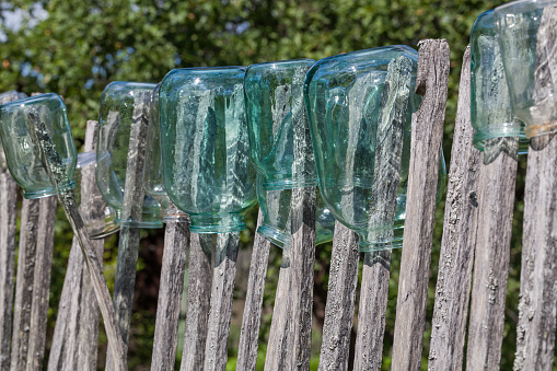 Clean glass jars hang on an old wooden fence on a green blurred background