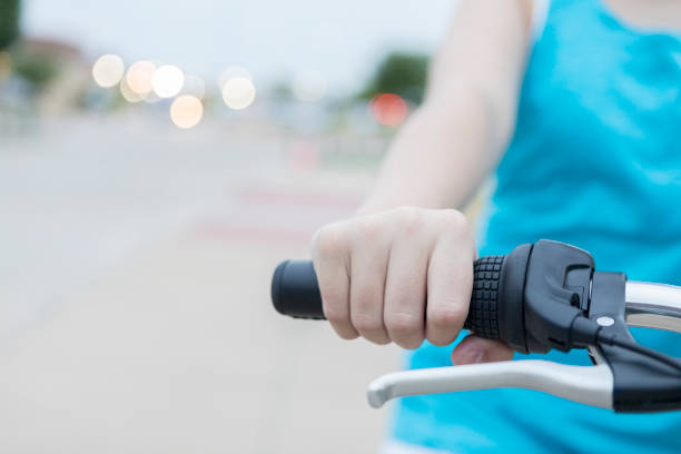 In this closeup, focus is on an older child's hand as she grips the handle on the handlebar of a bicycle.  She is riding down a sidewalk beside a street.