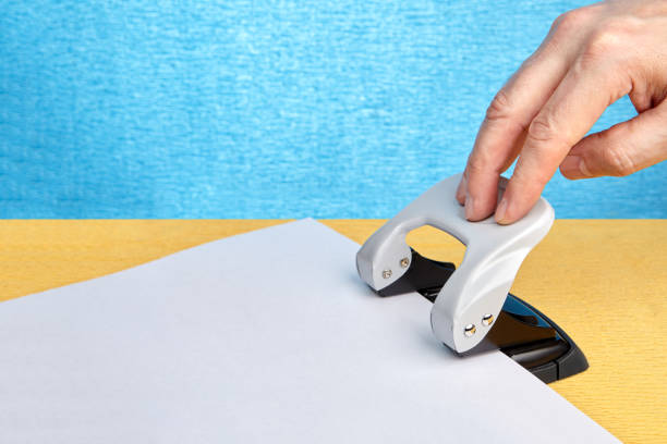 Hand preparing to press an office punch for making holes in paper.