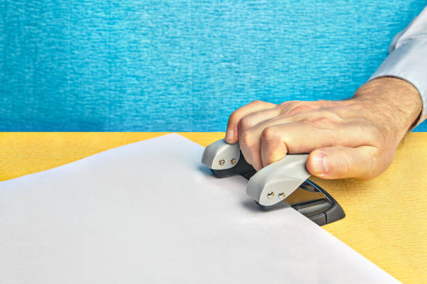 Man's hand strongly presses on a punch and makes holes in a paper.