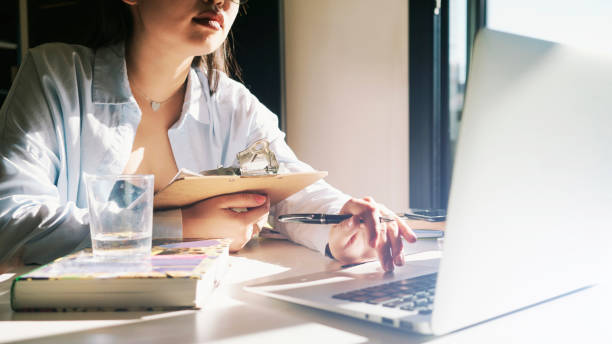 istock Student girl is reading textbook while sitting beside the big window on a sunny day. Young entrepreneur female is searching the information while preparing to the new product presentation. 1027830126