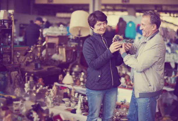 smiling man and his wife are visiting market of old things and looking collectible outdoors.
