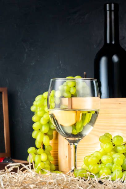 weiße weinglas und weiß gelb grün trauben beeren mit flasche wein korkenzieher für cork auf tisch im weingut konzept lebensmittel landwirtschaft ernte önologische herbst sommer. - berry fruit refreshment rural scene vertical stock-fotos und bilder