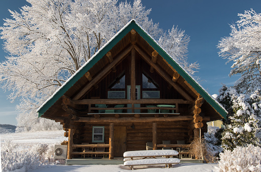 A log cabin in the countryside surrounded by snow covered trees during the winter.