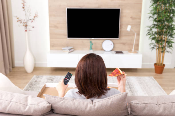 istock Single woman eating pizza and watching tv 1027876408