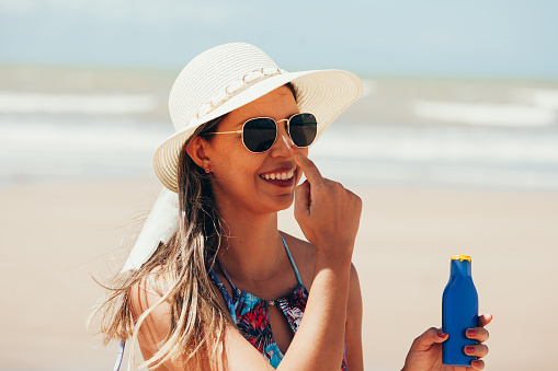 Sunscreen, sunblock. Woman putting solar cream on nose smiling beautiful summer day. Skincare. Girl applying sun cream