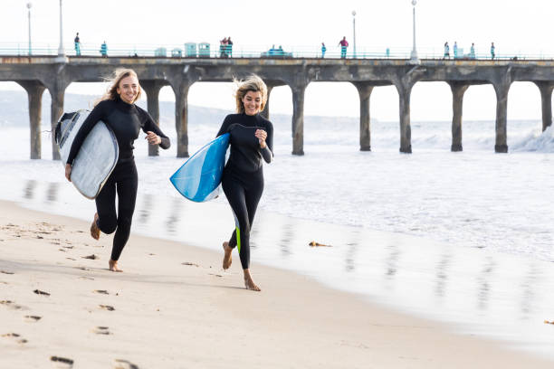 frauen gehen mit surfbrettern am strand - santa monica surfing beach city of los angeles stock-fotos und bilder