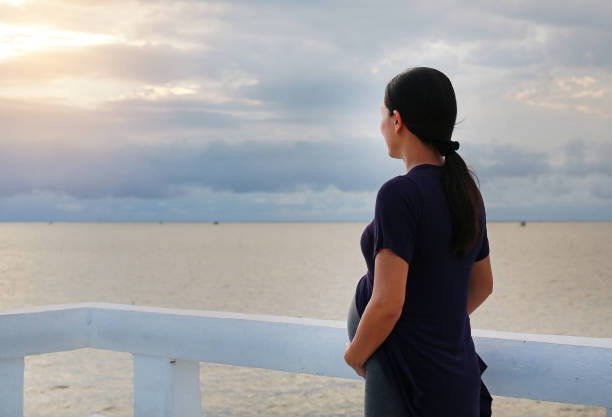 istock Pregnant woman standing on seashore with relaxed expressions. 1027921720