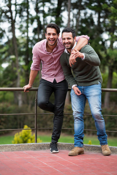 Two Latino friends, between 25 and 39, laughing happily on a balcony, holding each other, watching something very funny and fun