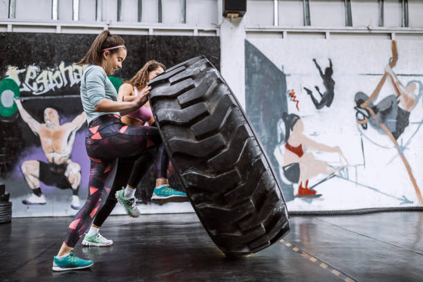 Group Of Young Women Flipping Tire On Cross Training In Gym