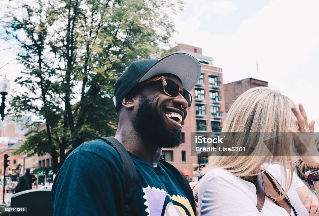 Love is Love Cute couple in sunglasses, man is black, African American, woman is a white blonde. they are outdoors in an urban setting, laughing at something off camera, a street performer in Boston, candid, smiling, fun, a couple maybe traveling Friendship Stock Photo