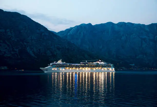 Beautiful Cruise ship at night in the see , mountains in background . Image contains noise
