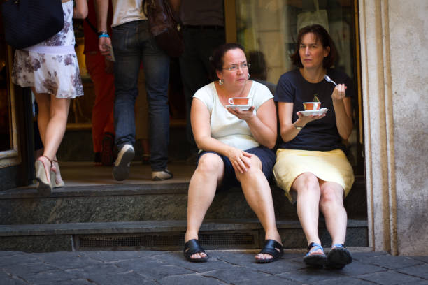 Rome, Italy: Two female tourists sit on a stoop with cups of coffee on Piazza della Rotunda, Rome.