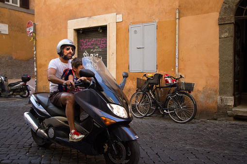 Rome, Italy: A father and son on a motorbike pass by on a street Rome’s Trastevere neighborhood.