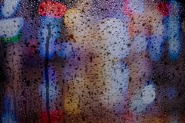 istock Rain drops on car window with light bokeh in night urban background. 1027998566