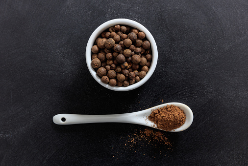 Allspice in porcelain bowl and spoon, black background