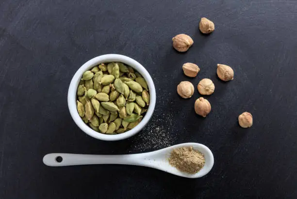 Cardamom in porcelain bowl and spoon, black background