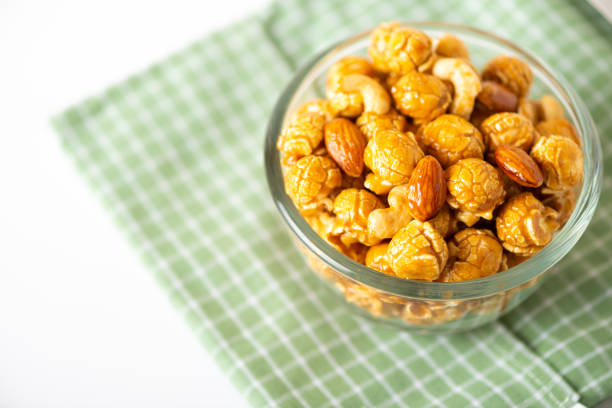 Caramel popcorn with cashew nuts and almonds in a white background, selective focus.