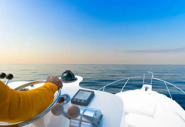 Photo of Hand of captain on steering wheel of motor boat in the blue ocean during the fishery day. Success fishing concept. Ocean yacht