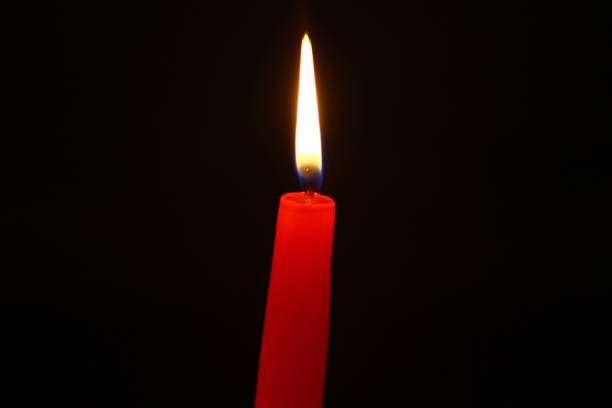 istock single wax burning red candle with bright fire against the heavy black background. 1028067492