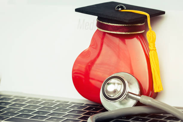 pós-graduação educação estudar hostpital médica internacional conceito: chapéu de formatura no coração vermelho com estetoscópio na mesa do computador de caderno - hostpital - fotografias e filmes do acervo