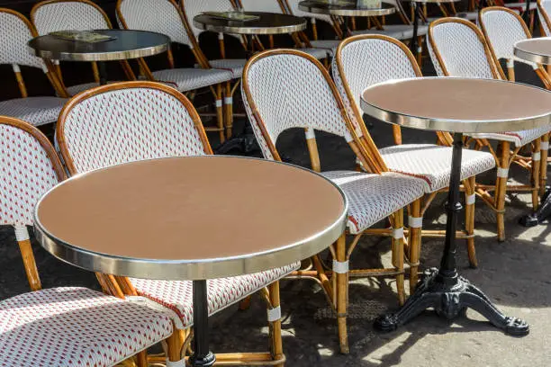 Photo of Typical tables and rattan chairs outside of a sidewalk cafe in Paris, France.