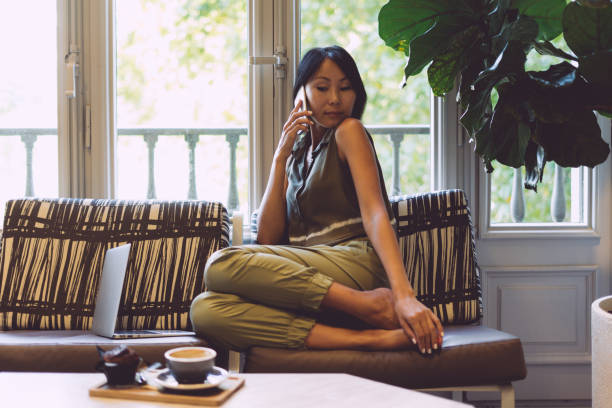 istock Attractive asian student is talking by mobile phone while sitting in a cafe with the modern interior. Beautiful entrepreneur female wearing casual clothes is making a business call during the break. 1028089252