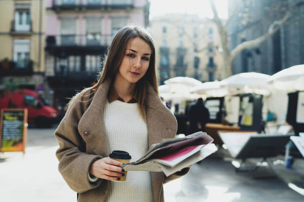 istock Successful designer happy to see her name mentioned in a city newspaper while walking down the street with a take away coffee. Young stylish hipster girl reading latest news in daily press. 1028091754