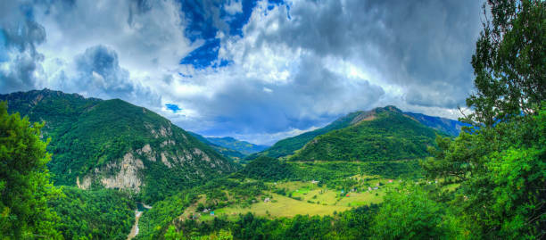 Dalin with houses and a river in the mountains \nA narrow mountain valley, called a gorge, passes a mountain road. The motorway seems like a thin light ribbon against the background of the mountains. All the rest of the space, where there is enough sight, is occupied by huge mountains, their slopes and peaks. Above them is only the sky.