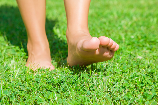 Young woman's barefoot walking on the fresh, green grass in sunny summer in the morning. Restful moment. Healthy lifestyle. Bright color. Front view. Close up.